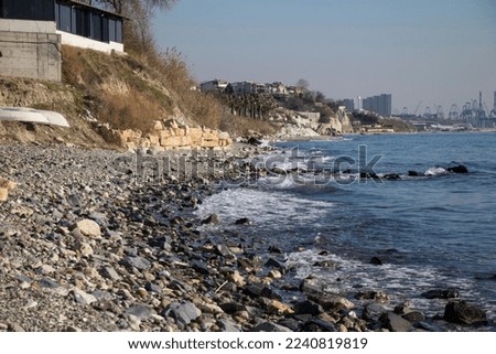 waves crashing on the beach covered with shells and round stones industrial structures in the distance harbor and cranes