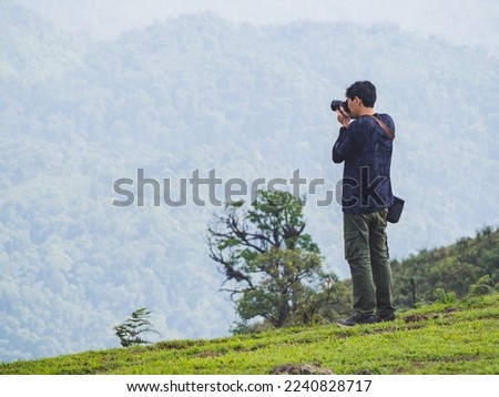Man hiker with backpack standing on top of the mountain and taking picture of valley
