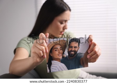 Upset woman ripping photo indoors, focus on picture. Divorce concept