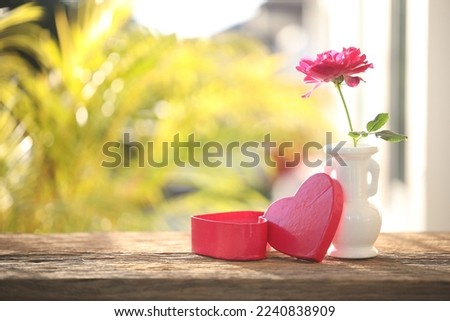 Red rose in a white vase and heart box on wooden table