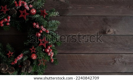 Close-up of beautiful Christmas wreath mad natural Christmas trees decorated with stars,cones and berries lies on old dark wooden boards,top view,copy space.Christmas and New Year banner.Wreath making