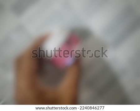 Defocused or blurred abstract background of a bottle of cosmetic or face cream as a treatment for face. It is held by a hand with a white wall as a background.
