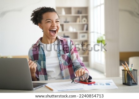 Excited happy overjoyed african high school girl student celebrating victory, got entrance letter, email with great exam test scores, good news, screaming yes, sitting at laptop computer at home.
