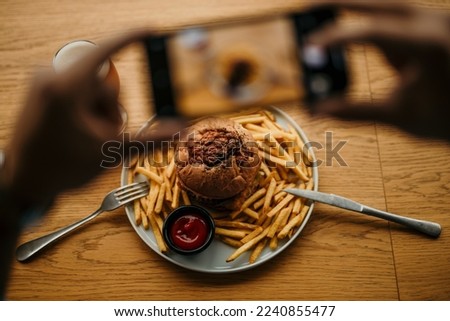 Top view of a male's hands taking a picture with a phone of his burger, french fries, and a beer pint. People photographing food concept. Focus on a food