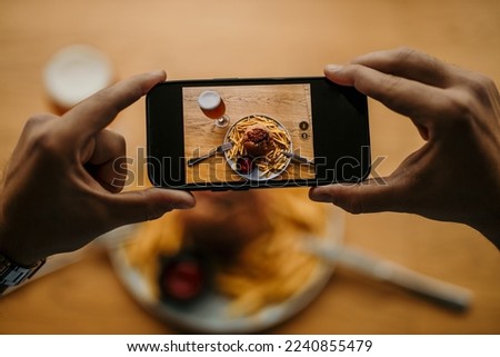 Top view of a male's hands taking a picture with a phone of his burger, french fries, and a beer pint. People photographing food concept. Focus on a food