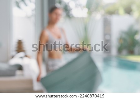 Fit woman with yoga mat in hands standing after yoga stretching exercises, meditation in beautiful villa view in open air near swimming pool Early morning time. Keep calm Defocused background