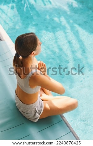 Millennial fit woman making yoga stretching exercises in open air in tropical yard on villa near swimming pool in Thailand early morning meditation. Active life concept Keep calm Vertical Top view