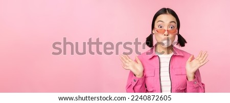 Stylish asian girl blowing bubblegum bubble, chewing gum, wearing sunglasses, posing against pink background. Copy space Royalty-Free Stock Photo #2240872605