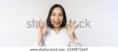 Close up head portrait of asian girl showing okay, ok sign and smiling satisfied, recommending, being pleased, praise and make compliment, white background.