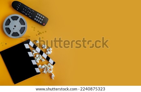 clapperboard, film strip and  popcorn,  tv remote on a yellow background. home movie night concept. flatlay. top view. copy space
