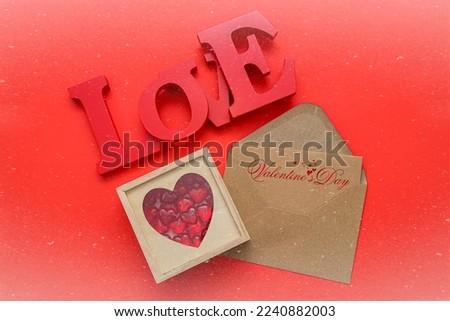 Red wooden letters in the word love with glass hearts in a wooden box and an envelope on red .