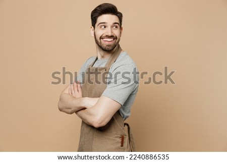 Young man barista barman employee wear brown apron work in coffee shop hold hands crossed folded look aside on workspace isolated on plain pastel light beige background. Small business startup concept Royalty-Free Stock Photo #2240886535