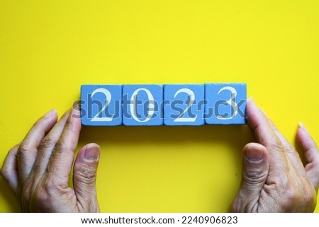 Man’s hand holding wooden cube number 2023 on yellow background, New Year concept.