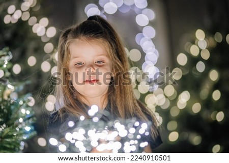 4 years old little girl looking up near Christmas lights 
