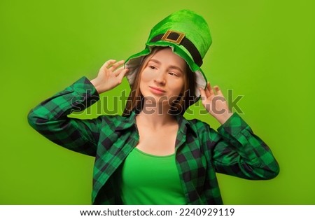 Young woman wearing green checkered plaid shirt, holding leprechaun hat and looking aside isolated on green background.

Happy St Patricks Day celebration concept. National Irish holiday.