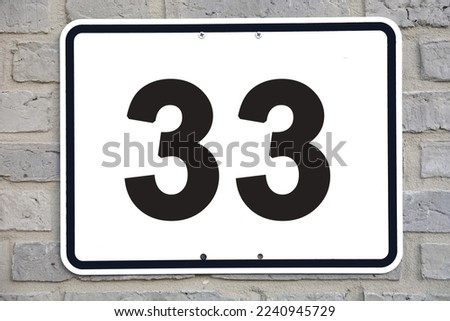 A white house number plaque, on a grey brickwall, showing the number  thirty three (33)
