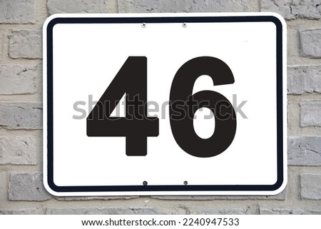 A white house number plaque, on a grey brickwall, showing the number forty six (46)