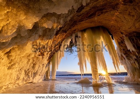 Lake Superior Ice Cave at Sunrise. The sun crests the horizon and shines through hanging ice curtains as it rises and illuminates the interior of a cave on Grand Island in Michigans Upper Peninsula.