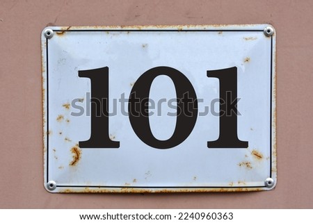 A white house number plaque, on a light red wall, showing the number one hundred one (101)