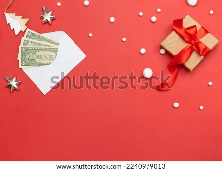 A red Christmas card, an envelope with dollars, a gift, stars, snowflakes. Christmas background with space for copy, Christmas decorations, gift decorated with red ribbon, white envelope with money
