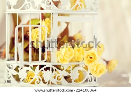 Close up of a decorative cage with yellow flowers in it, rounded by champagne color satin.