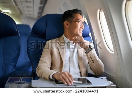 Successful and handsome Asian businessman in formal business suit is on his private jet, looking out the window, taking a flight for his business trip. Royalty-Free Stock Photo #2241004491