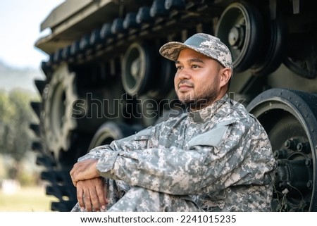 Asian man special forces soldier against on the field Mission. Commander Army soldier military defender of the nation in uniform sitting near battle tank while state of war. Royalty-Free Stock Photo #2241015235