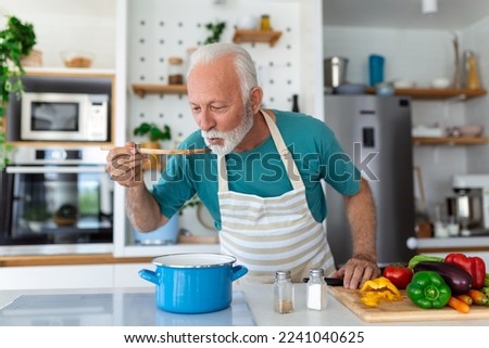 Happy retired senior man cooking in kitchen. Retirement, hobby people concept. Portrait of smiling senior man holding spoon to taste food