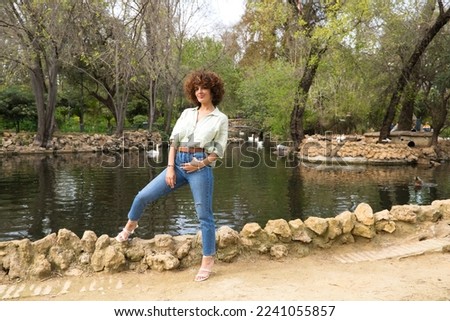 beautiful woman with curly hair is standing in front of a pond of ducks and swans in the park. The woman is on holiday in Seville and enjoys the scenery and the holiday. Holiday and travel concept.