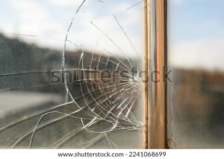 Dirty broken glass with cracks from stone hit or beak from bird flying near creation. Unwashed window with view of picturesque nature with metal partition and traces of breakage needs to be replaced  Royalty-Free Stock Photo #2241068699