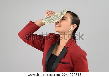 Portrait of young asian woman in officer costume use wireless earphone and hold fan banknote or dollars bill in hands, free space to put products for advertisement isolated on white background
