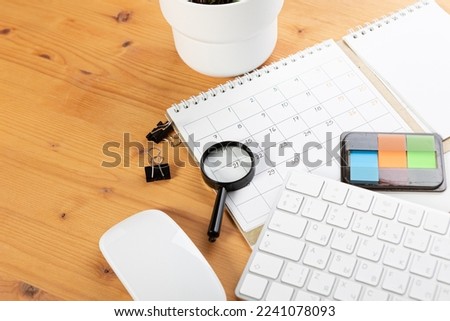 Calendar and reminders with magnifying glass, work from home online. glider on desktop with mouse and pen, keyboard. mark a holiday trip or plans in a diary at the office desk. 2023 calendar