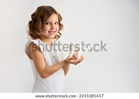 Little girl holding tooth on a white background with copy space. Portrait of happy girl with white teeth, close-up