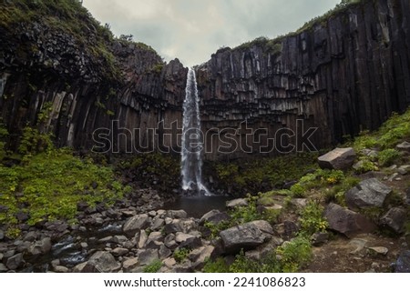 Narrow waterfall on high cliff landscape photo. Beautiful nature scenery photography with grey sky on background. Idyllic scene. High quality picture for wallpaper, travel blog, magazine, article
