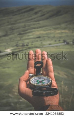 Close up woman holding compass concept photo. Navigation at hike. First view person photography with green highland on background. High quality picture for wallpaper, travel blog, magazine, article