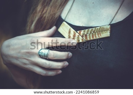 Close up woman with metal ring and wooden pendant concept photo. Side view person photography with dark background. High quality picture for wallpaper, travel blog, magazine, article