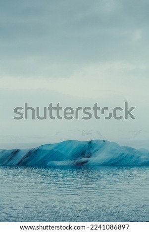 Patterned iceberg in water landscape photo. Beautiful nature scenery photography with cloudy sky on background. Idyllic scene. High quality picture for wallpaper, travel blog, magazine, article