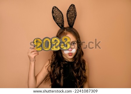 A girl with openwork rabbit ears closes her eye with the number 2023 of the new year, sends an air kiss