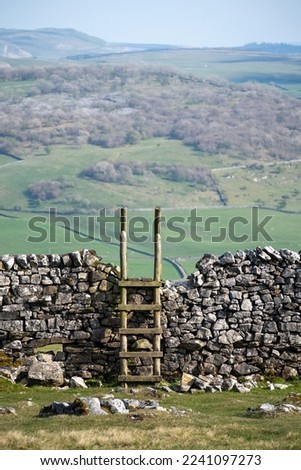 Traditional stile in a dry stone wall in the Yorkshire Dales, with classic limestone countryside landscape in the background on a beautiful day in England. Royalty-Free Stock Photo #2241097273