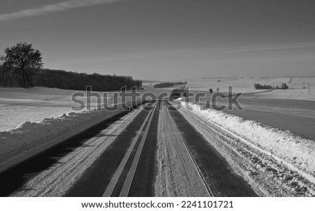Winter road. Winter landscape winding road. Snowy winter on the countryside view, black and white picture. Road leading through snowy fields. Drifts on the road.


