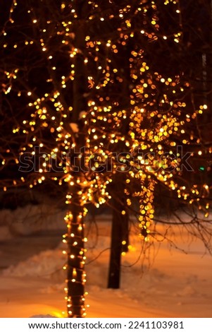 The tree on the street is decorated with garlands with yellow light, festive illumination, out of focus, golden bokeh, festive mood, winter, new year and christmas, vertical photo, blurry, shine, snow