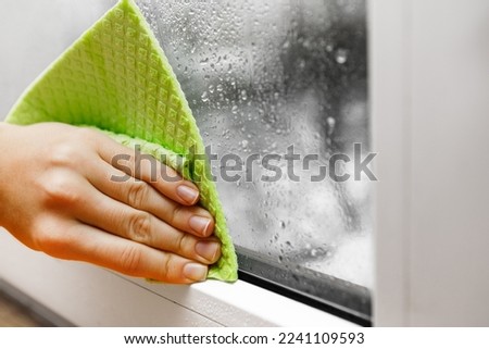 high humidity in the house. hand wipes off water condensation from plastic window glass in the room Royalty-Free Stock Photo #2241109593