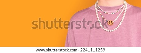 Banner with multicolored pearl beads on a young woman in a pink t-shirt in front of yellow background. Selective focus.