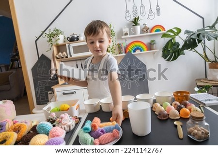 Male baby chef in apron posing at childish kitchen cafe public catering with food sweet delicious and drink toys imitation. Happy child boy cookery worker at gourmet cuisine playthings home interior Royalty-Free Stock Photo #2241142767