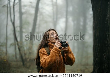 Anticipating female hiker holding a photo camera and taking nature pictures during a foggy and rainy day