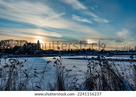 Amazing beautiful view of sunset in the bay at the port city of Gustavsberg near Stockholm in Sweden. White clouds. The rays of the sun formed a halo around. Ice covered the bay.