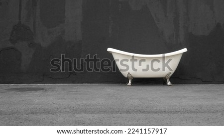 White acrylic bathtub on chrome legs on the street against a dark gray wall. Copy space.           