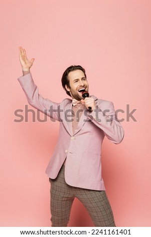 Cheerful host of event singing while holding microphone on pink background