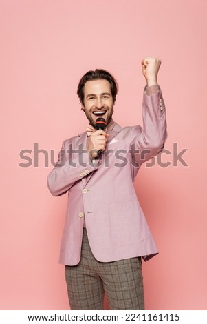 Excited host of event showing yes gesture and talking at microphone on pink background
