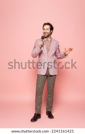 Full length of stylish host of event holding microphone on pink background